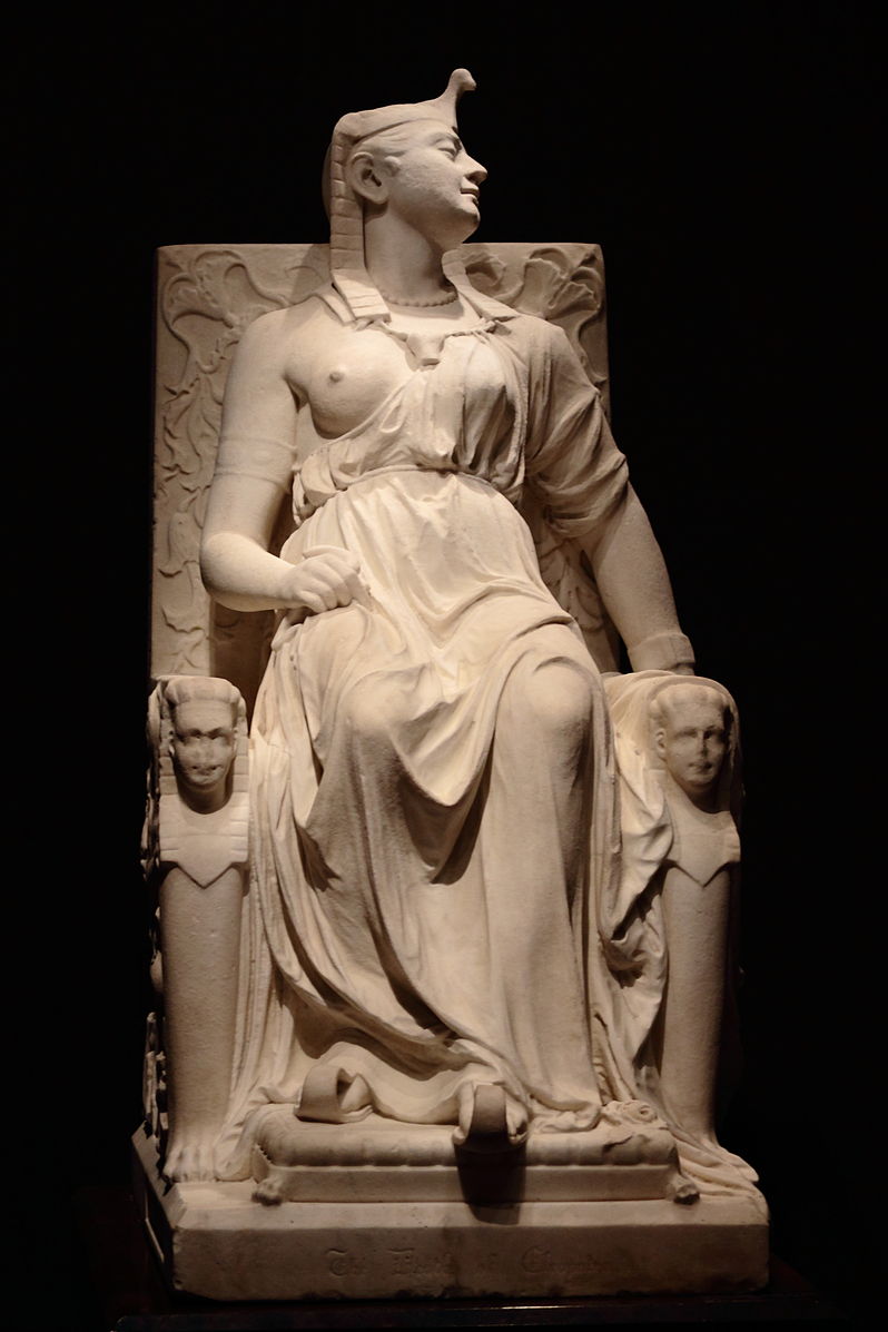 A marble statue of a woman sitting in a chair with a headdress and long flowing robe