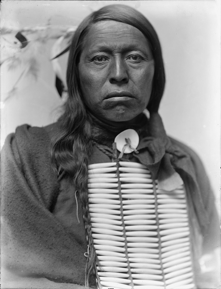 A portrait of a man with long hair wear traditional native clothing