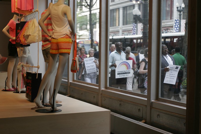 Marchers brandissant des pancartes sur lesquelles on peut lire « Personne ne devrait mourir pour la mode » et « Sauvez des vies » devant la vitrine d'un magasin de vêtements