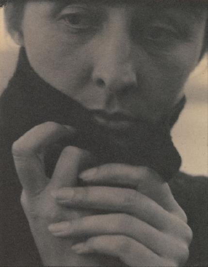 a woman with a black sweater with her hands clasped together in front of her neck