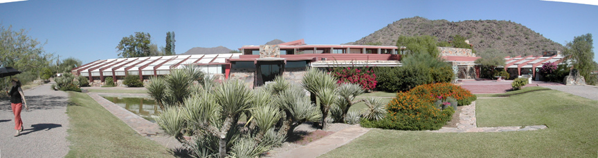 A house built in a desert setting with large white roofs and red metal beams