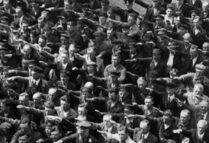 Foto histórica de un grupo de hombres realizando el saludo nazi en la Alemania nazi. Una persona se niega a hacerlo y de pie con los brazos cruzados.