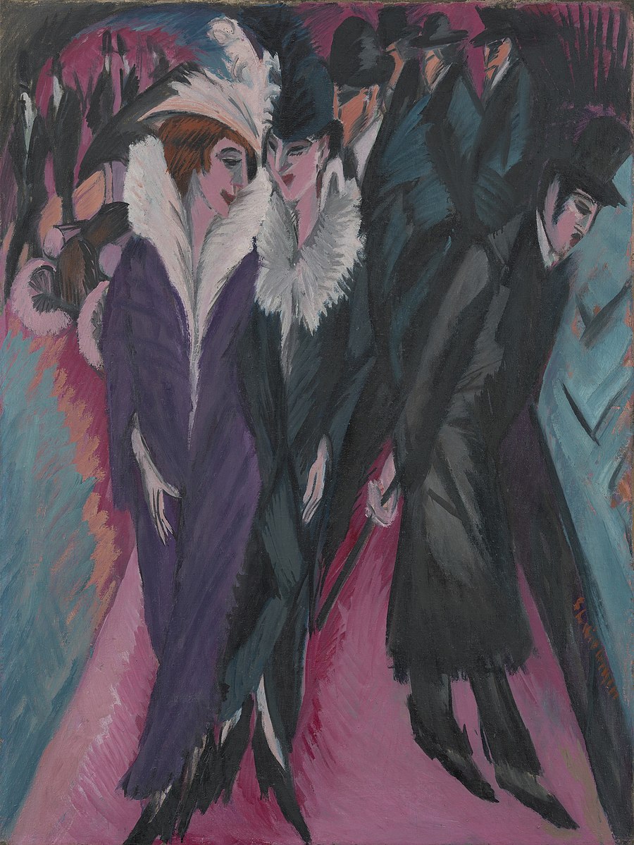 Two women and a man in a room of other people wearing dresses and tuxedo