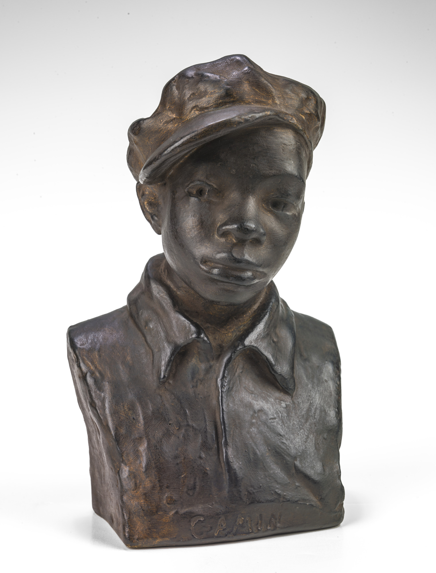 A bronze statue of a young boy with a hat on his head and a zipped up jacket