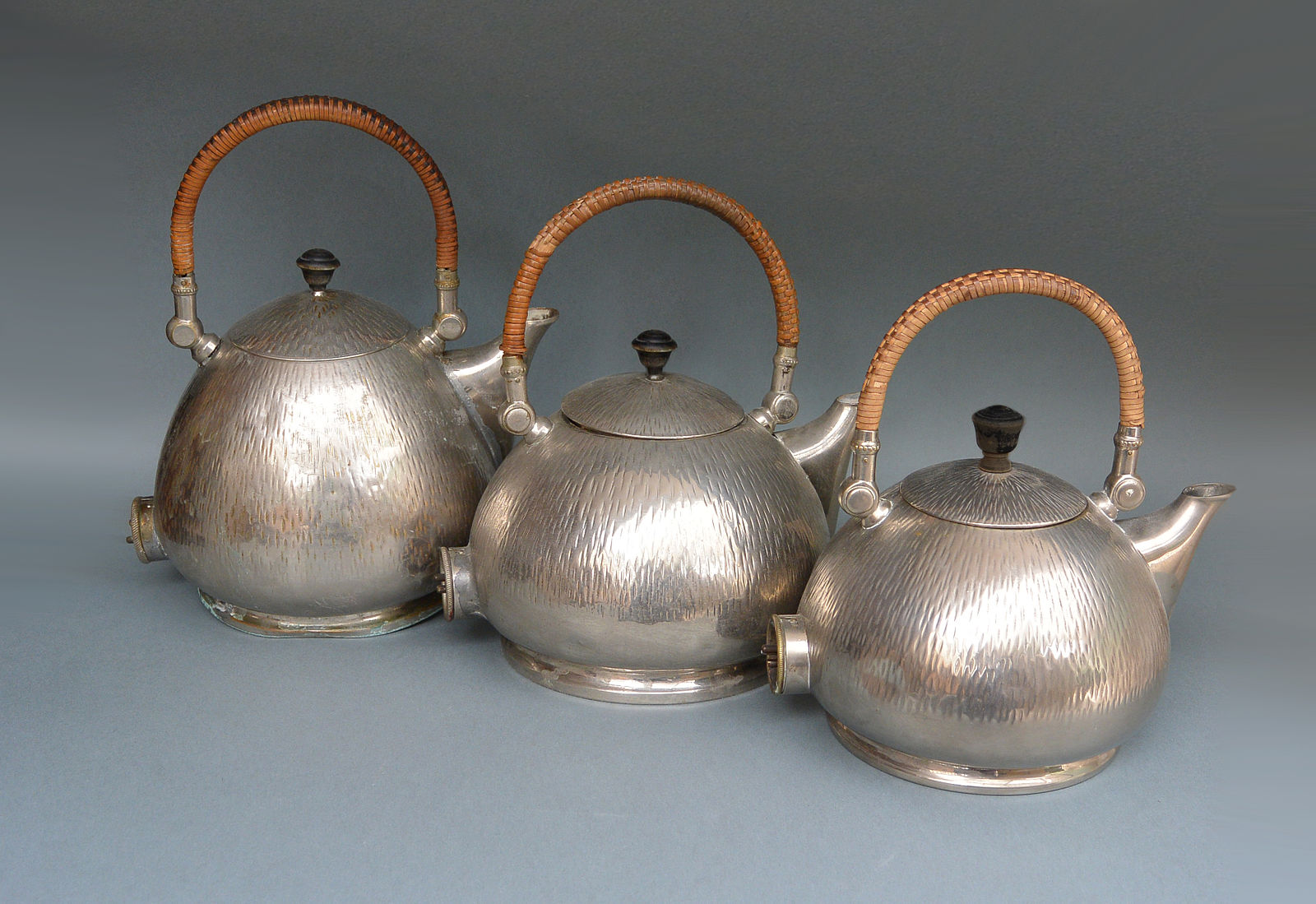 Three silver teapots with woven reed handles