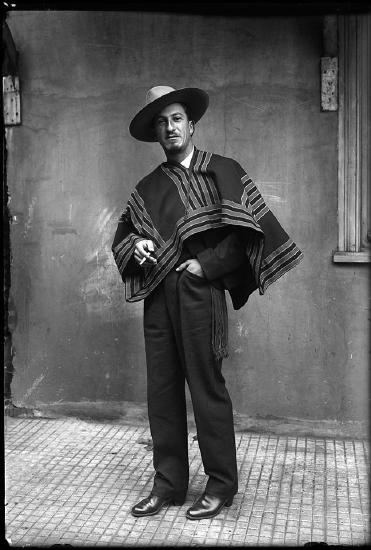 Photograph of a man wearing black pants and a striped jacket with a hat