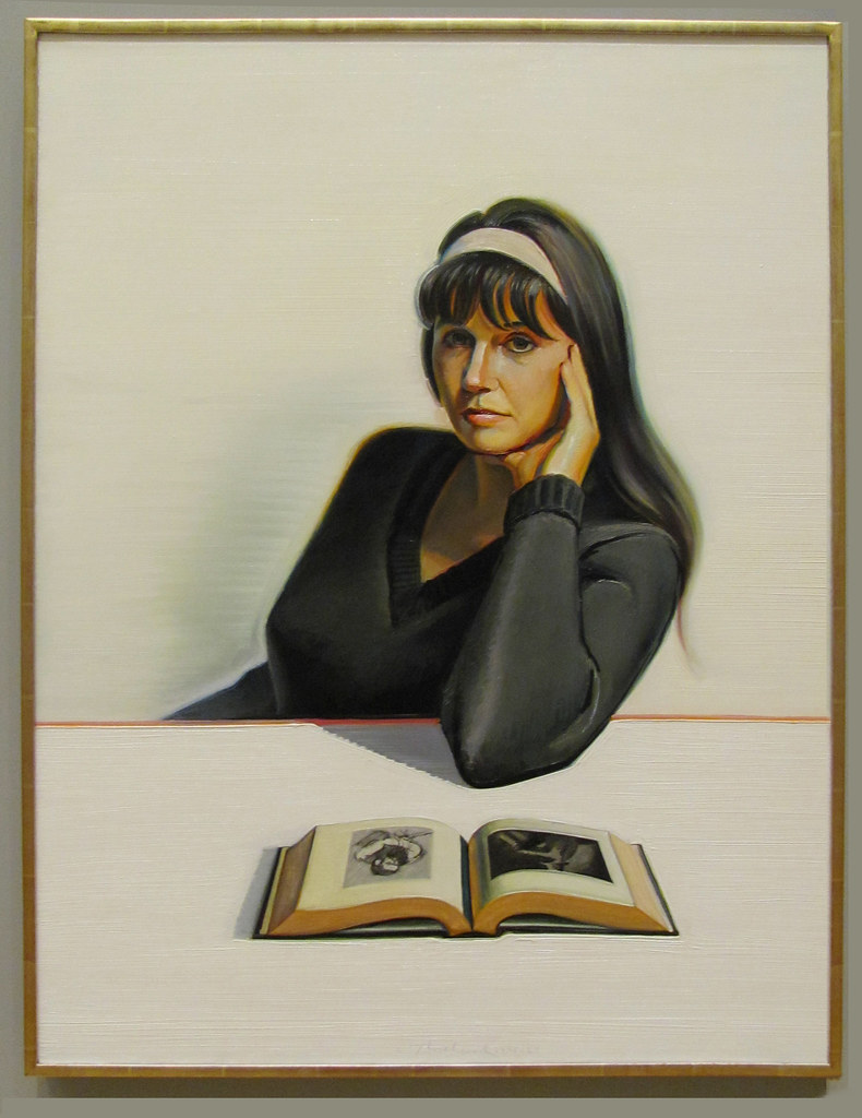 a woman sitting at a desk in a black dress with a book
