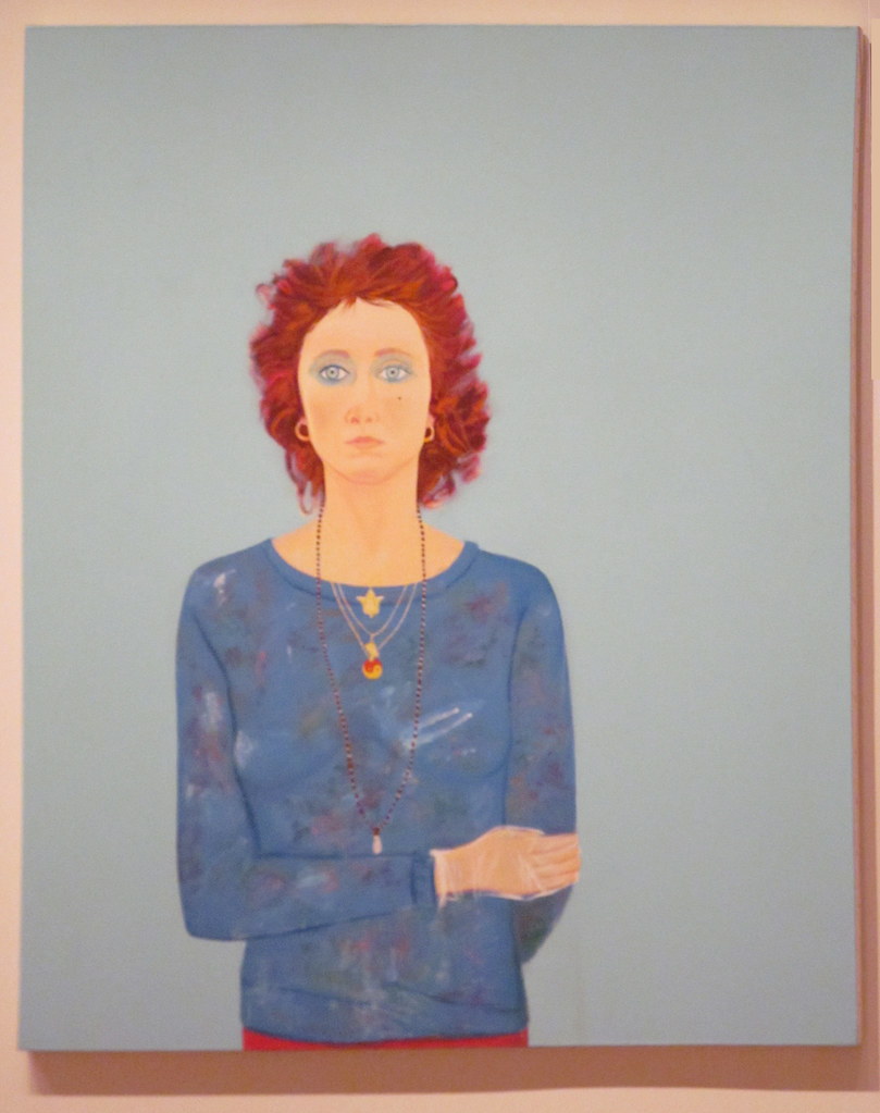 A woman with a blue shirt and red hair against a grey background