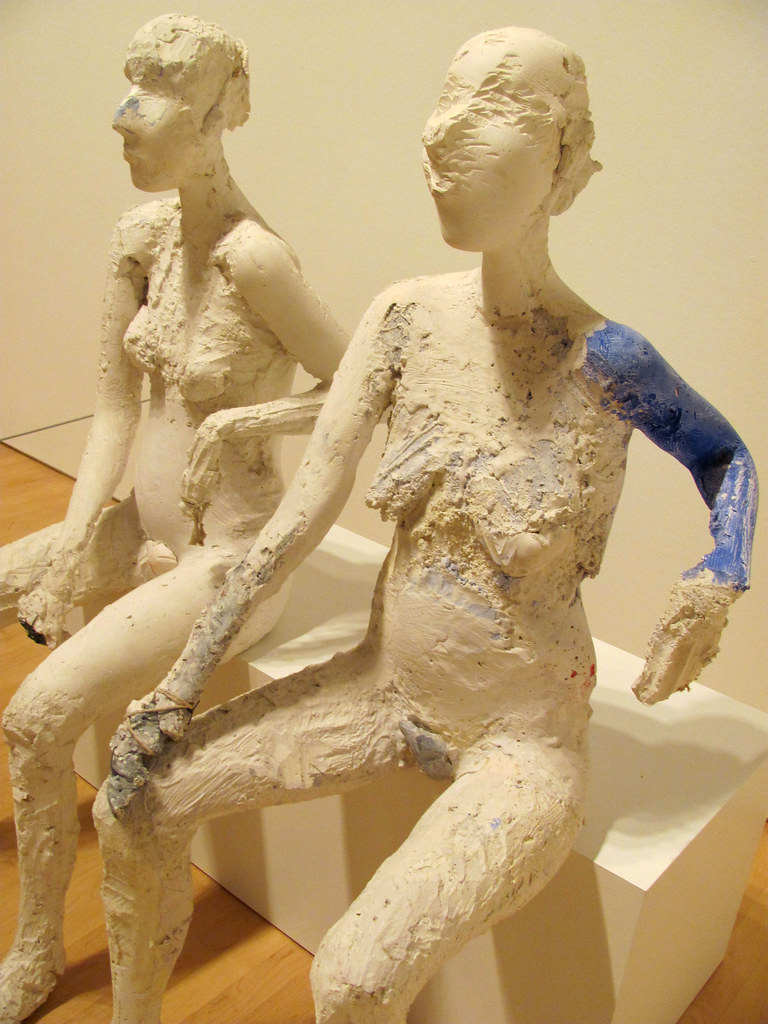 Two nude women statues, one with a blue arm