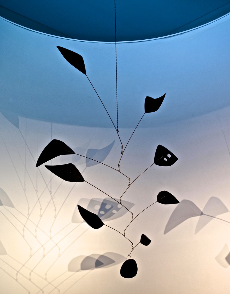 A black hanging sculpture against a blue and white backdrop