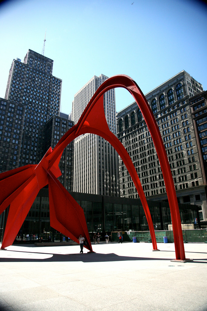 A large red sculpture set in concrete outside in a city space