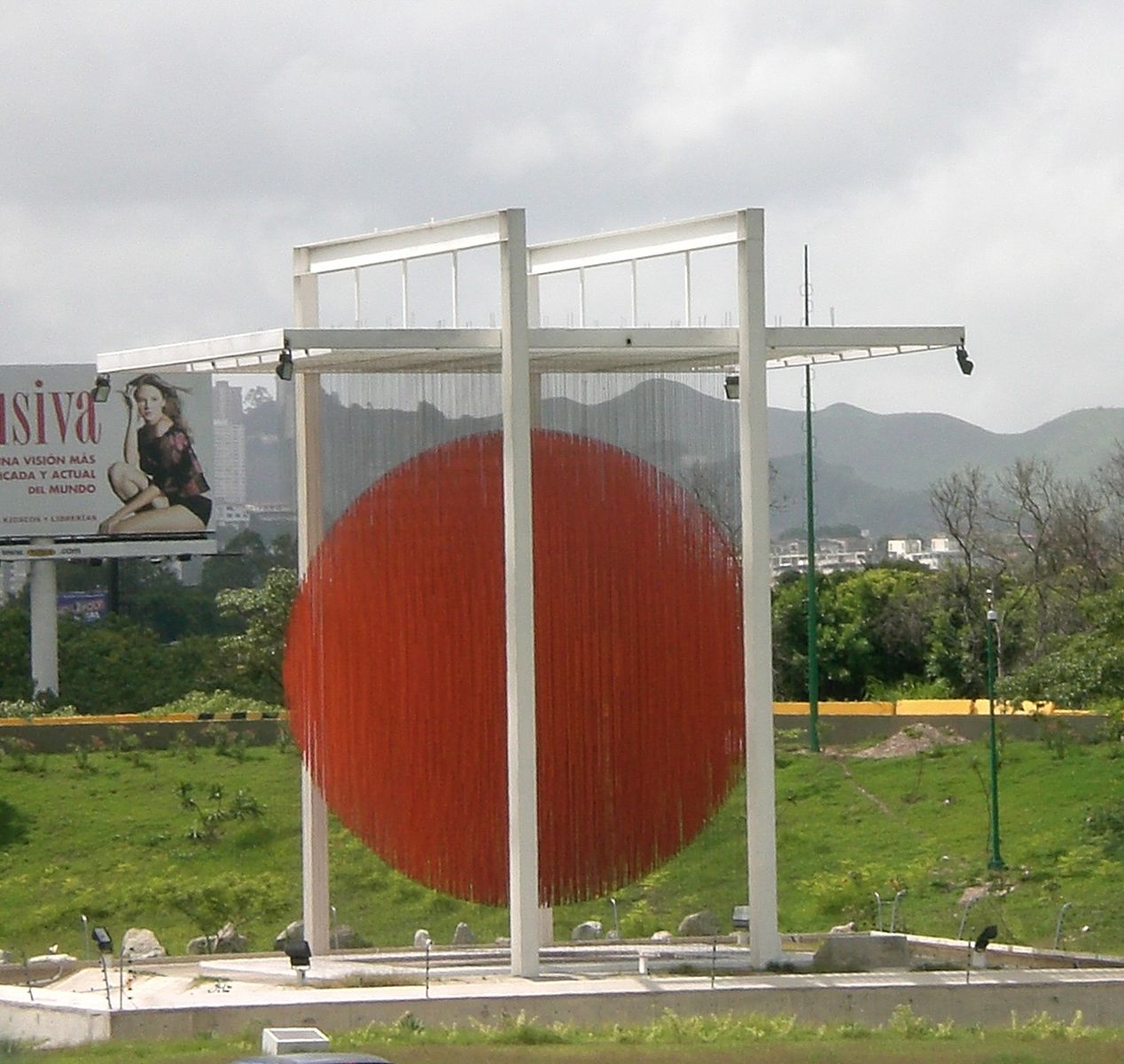A large metal sculpture shaped in a box with a circle of red rods hanging