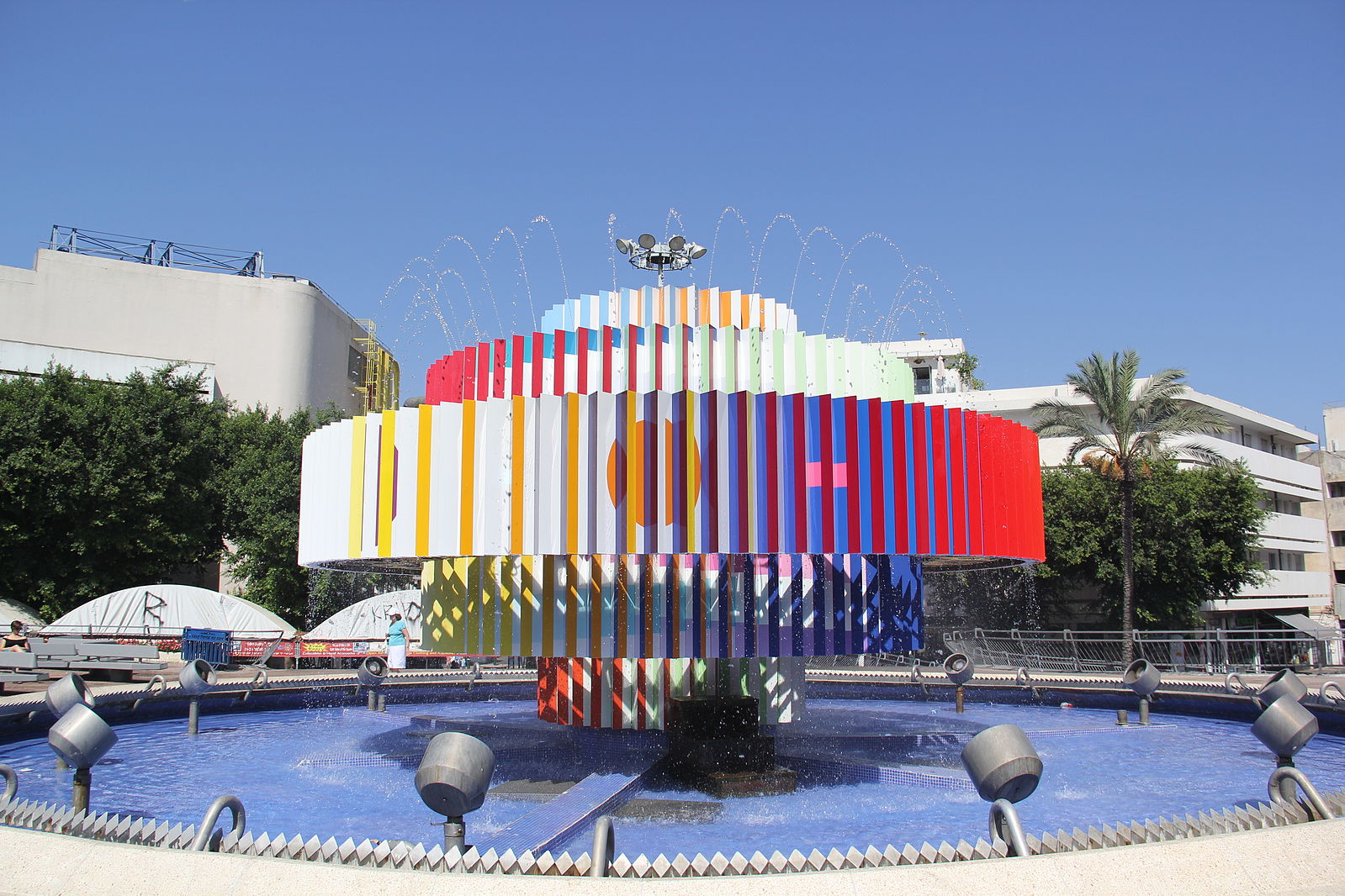 A circular water fountain with many colors spewing water into a pond