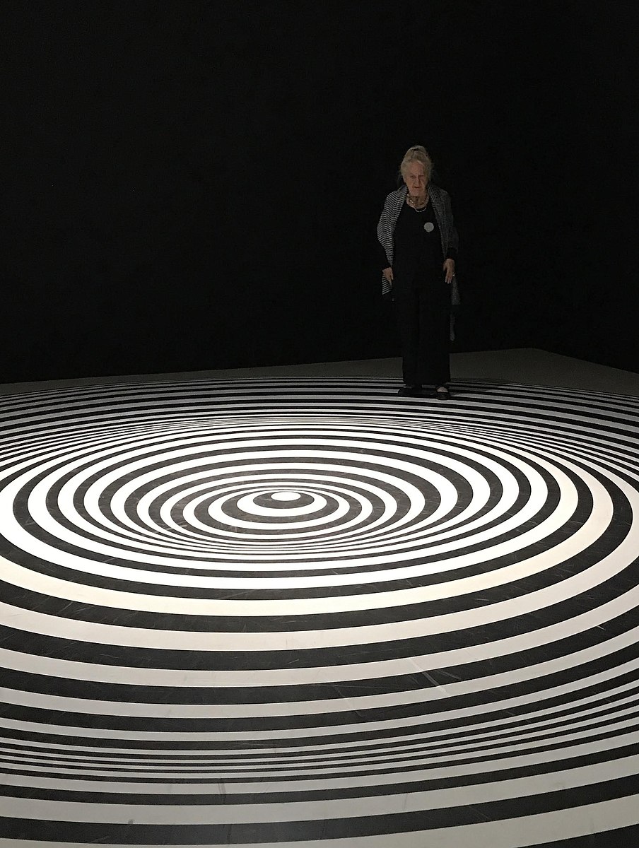 A woman in black standing on a floor with of black and white circles