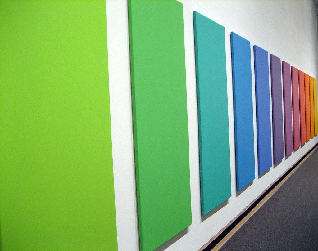 A rainbow installation of rectangle boards each painted with a color of the rainbow mounted on a wall