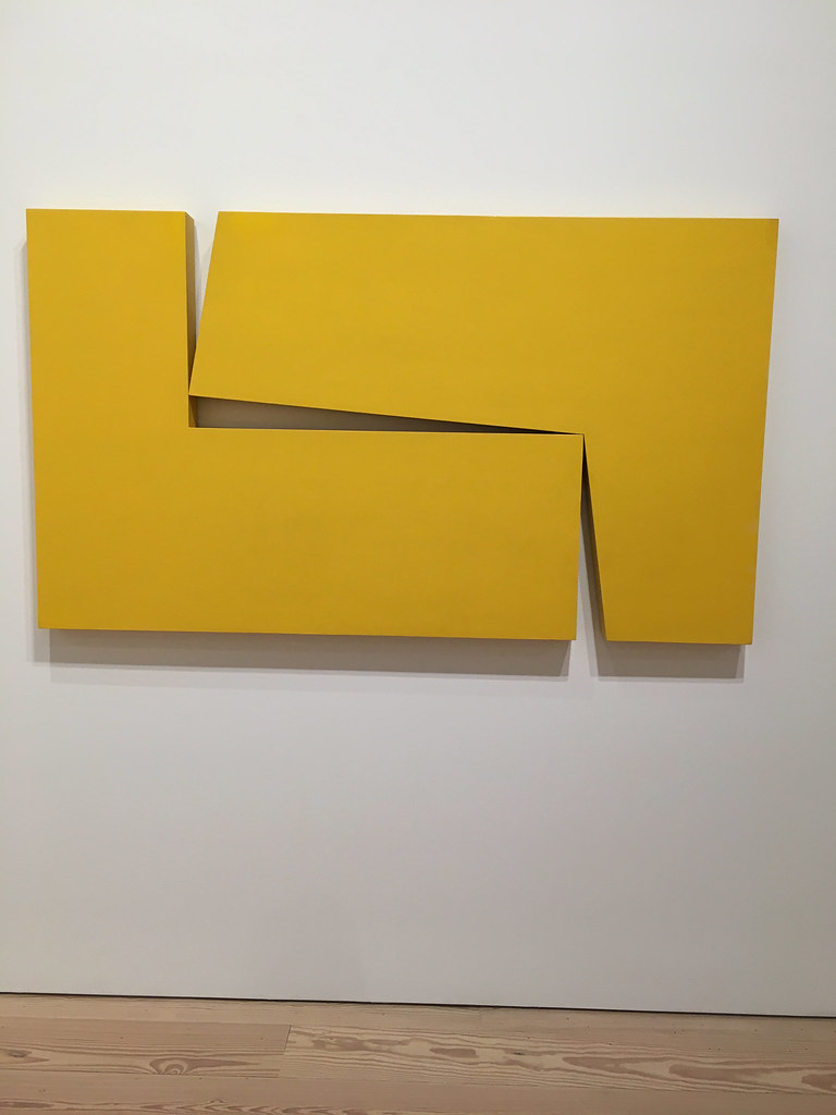 Dos objetos amarillos en forma de “L” colgados en una pared blanca