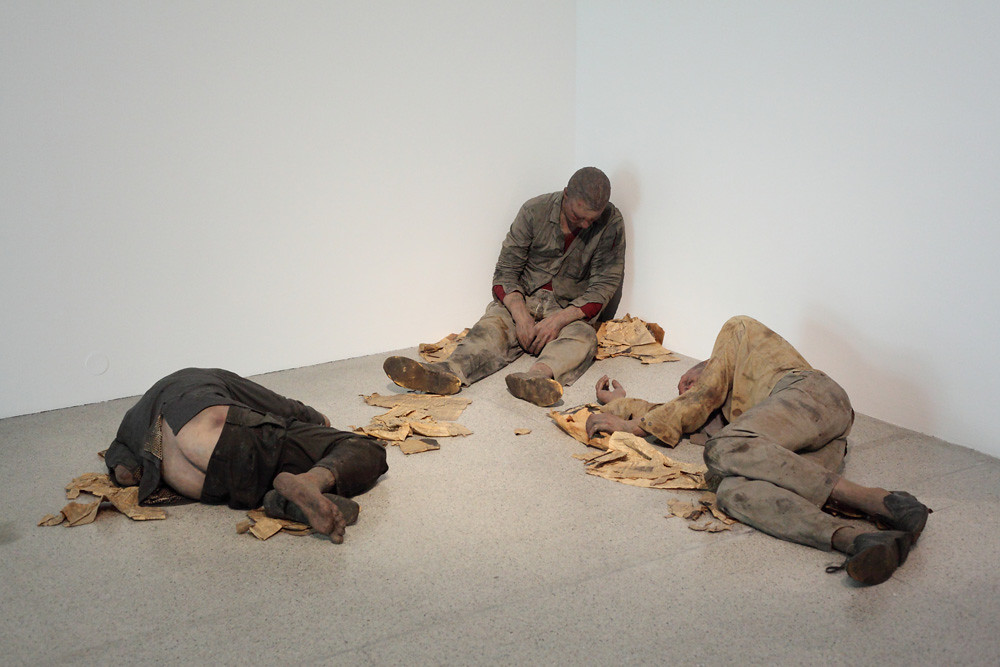 Two men in old clothes laying on the floor and one man in old clothes leaning against the wall
