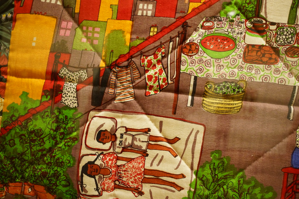 a quilt with two kids lying on the roof of a building with a clothes line and dinner table