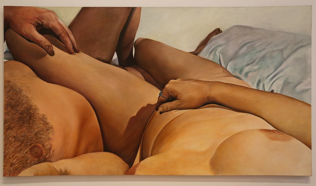 Two nude people laying on a bed in an embrace