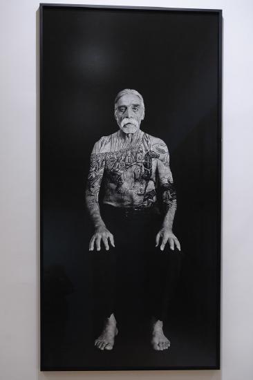 an older man sitting on a chair with a tattoo on his chest and arm