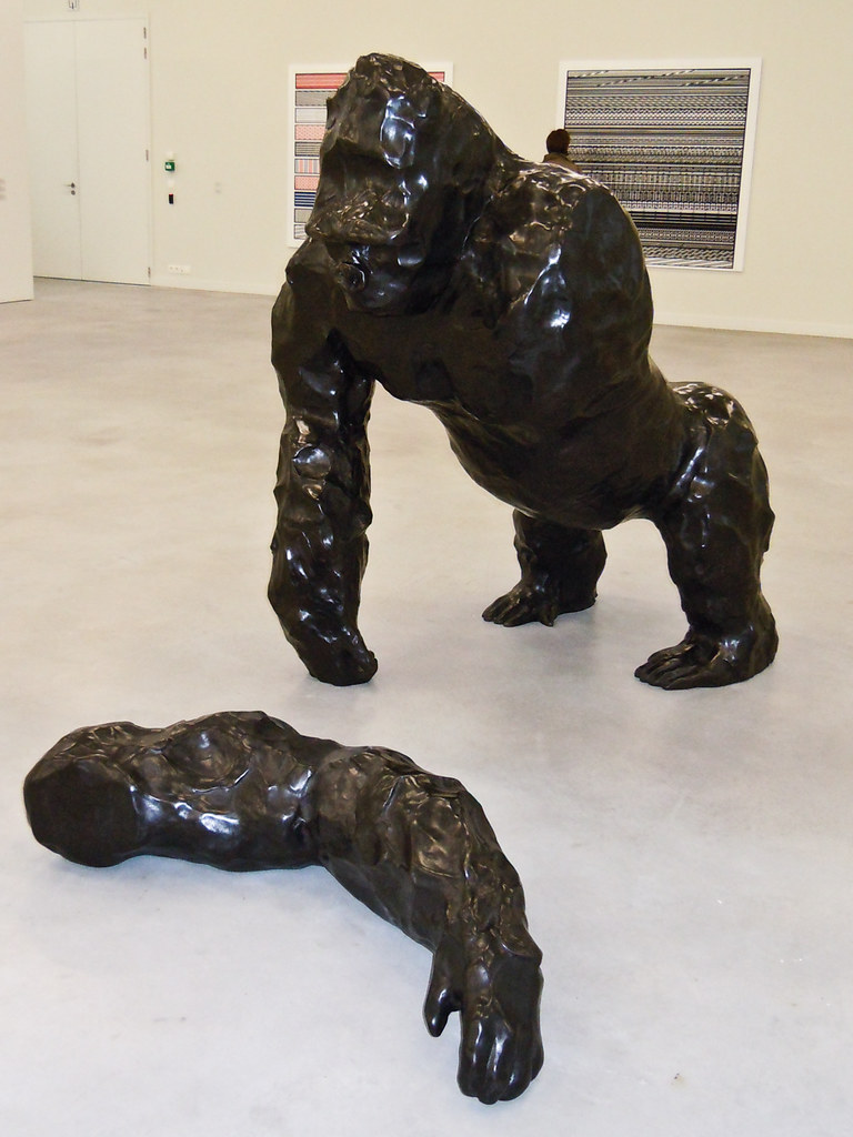 A black bronze statue of a monkey with his arm cut off laying on the ground
