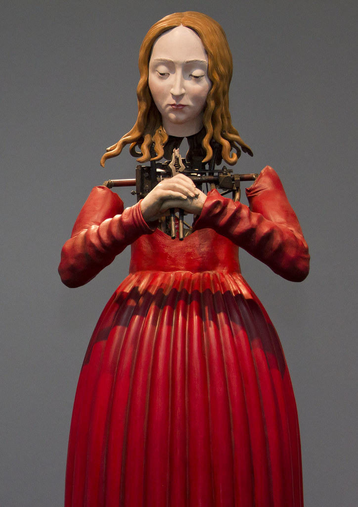 A robotic woman in a red dress clasping her hands over each other 