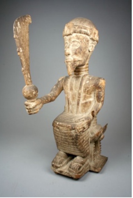 a carved man sitting in a chair holding a large sword