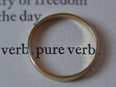 A wedding ring laid on top of the words "verb pure verb" on a printed page.