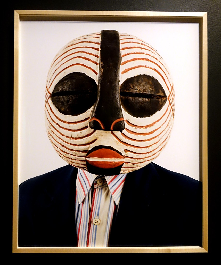 un hombre con máscara con líneas blancas y rojas, grandes ojos negros y nariz negra