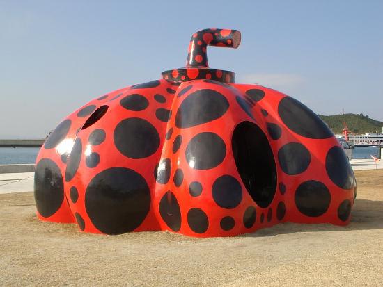 a very large red pumpkin with black polka dots set on the sand by the ocean