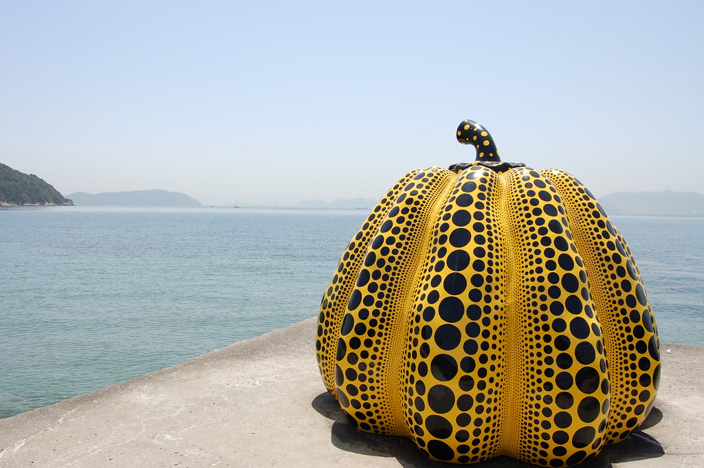 Large yellow pumpkin with black polka dots in sand at the beach