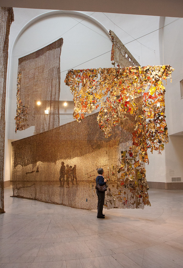 a large scale installation with 3 main parts made of gold and red bottle caps