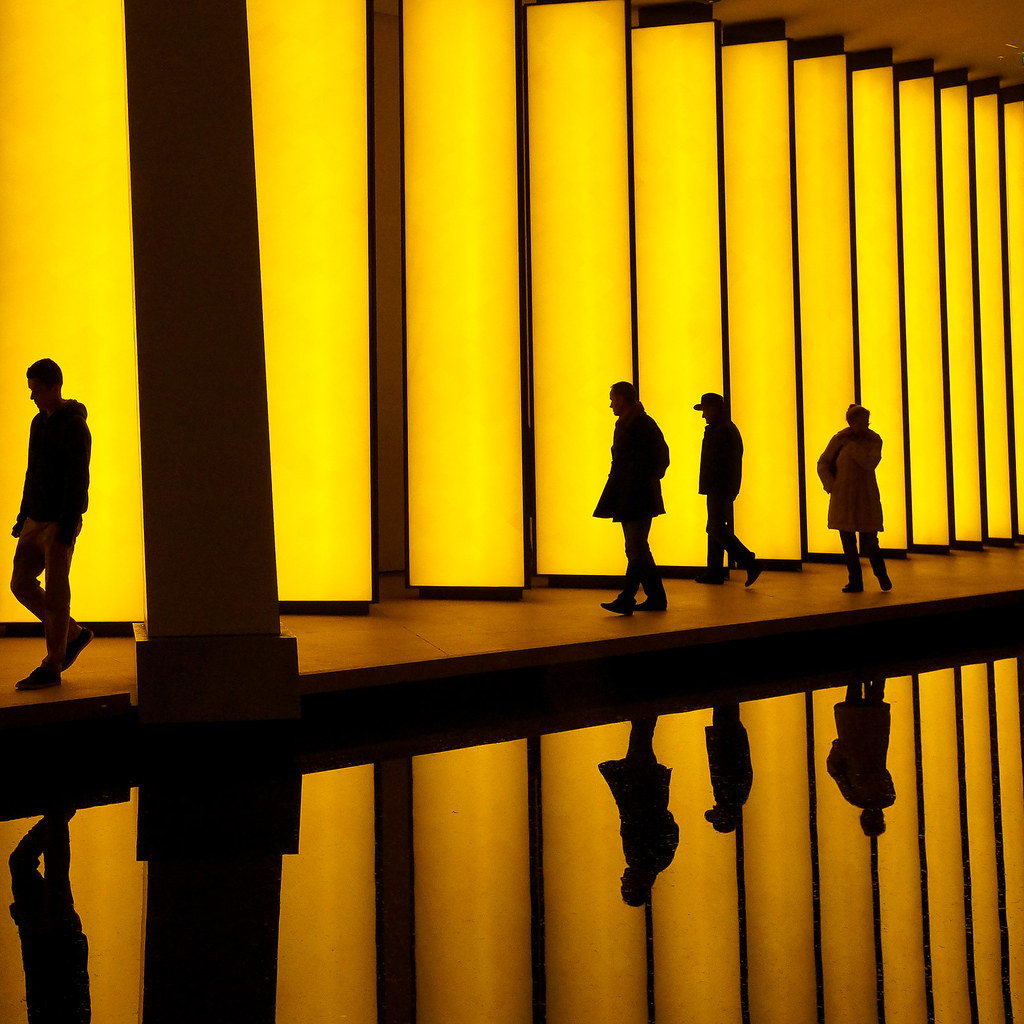 a series of yellow lights on a wall that reflect on a pool
