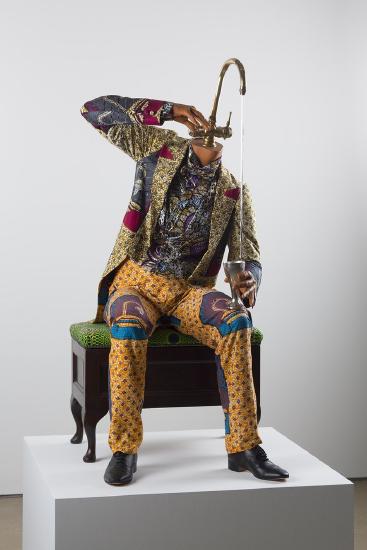 a man in brightly colored clothes sitting on a bench with a faucet for a head and water running into a cup