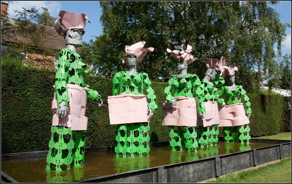 abstract sculptures of women standing in a pond in green and pink metal