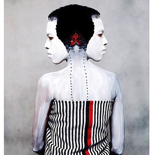 a woman standing with her back towards us with a black and white shirt and two heads each turned to see the viewer