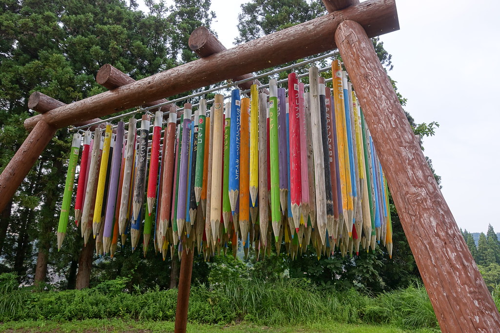 a very large sculpture of colored pencils hanging from a support of wood beams
