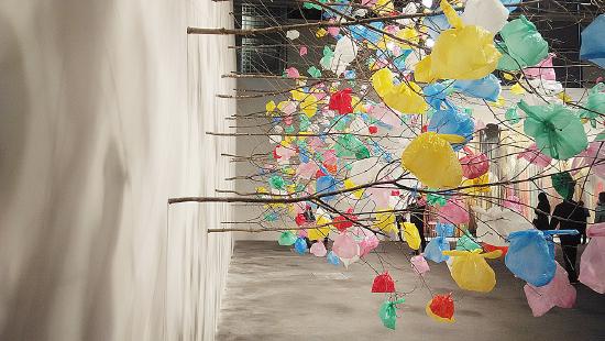 limbs of trees sticking out of the wall with colorful plastic bags tied to the ends