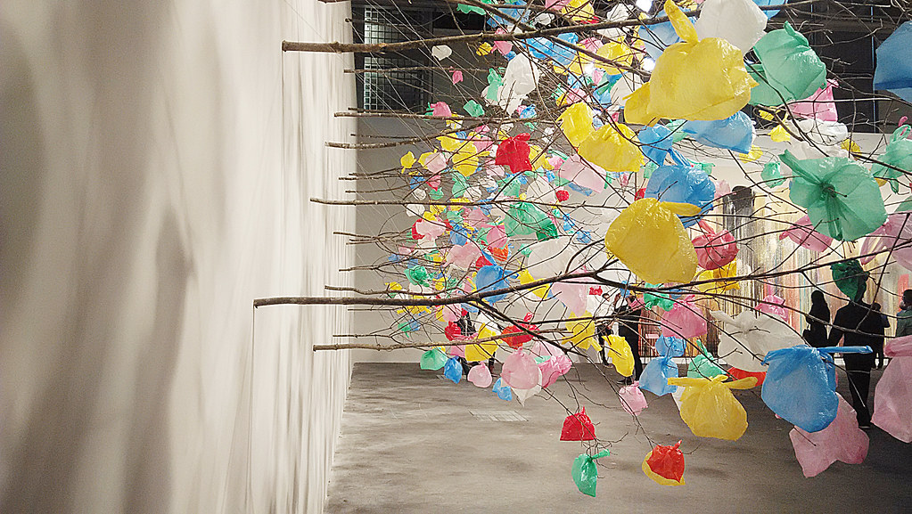 limbs of trees sticking out of the wall with colorful plastic bags tied to the ends