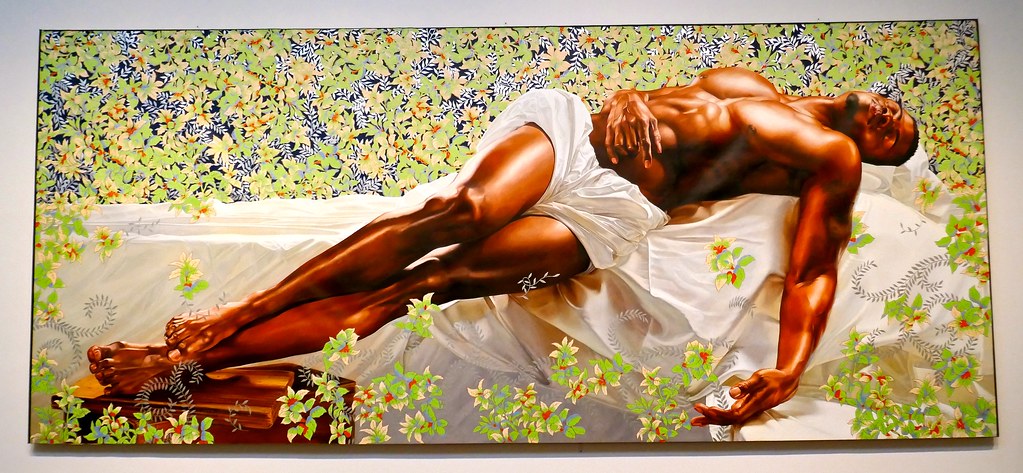 man wrapped in a white sheet laying on a bed surrounded by flowers