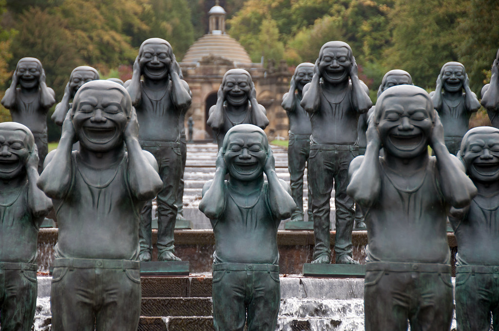 several bronze men standing while laughing and covering their ears with their hands