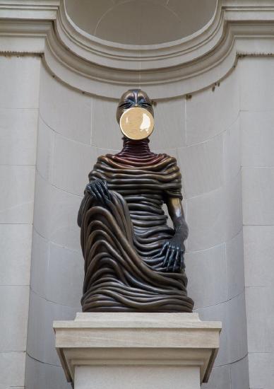 a bronze sculpture of a person sitting with one hand on its knee
