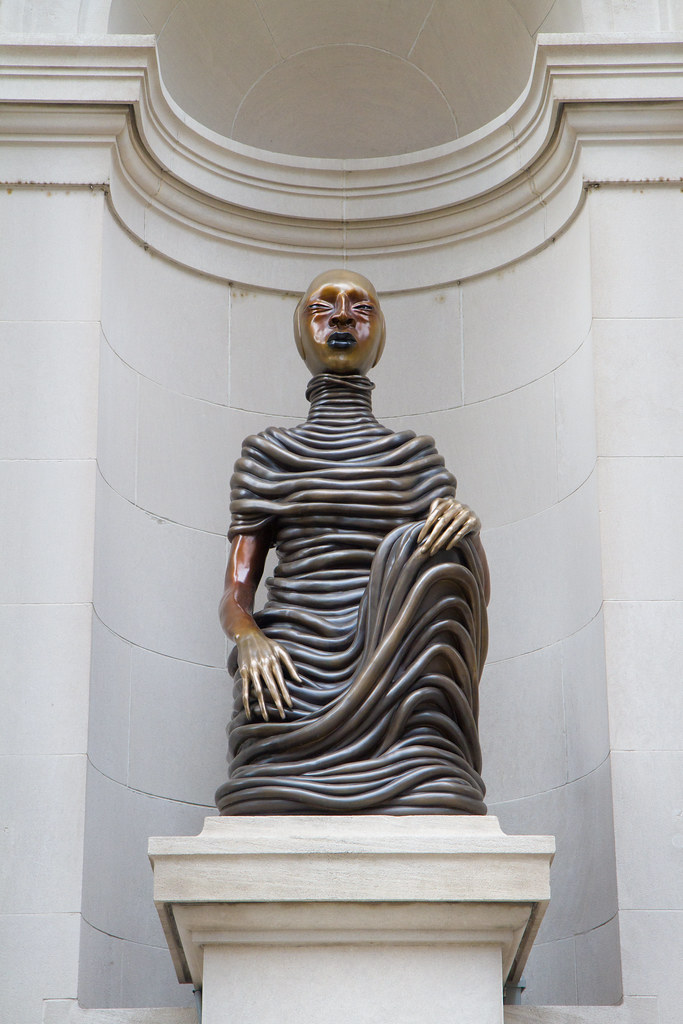 una escultura de bronce de una persona sentada con una mano sobre la rodilla