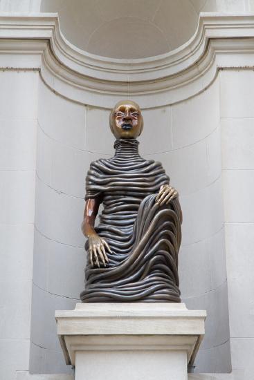 a bronze sculpture of a person sitting with one hand on its knee