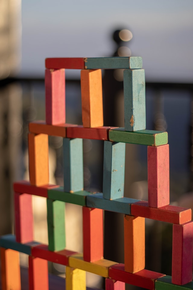 Blocos de construção de madeira coloridos dispostos em uma pirâmide com espaços entre os blocos e sem nível superior.