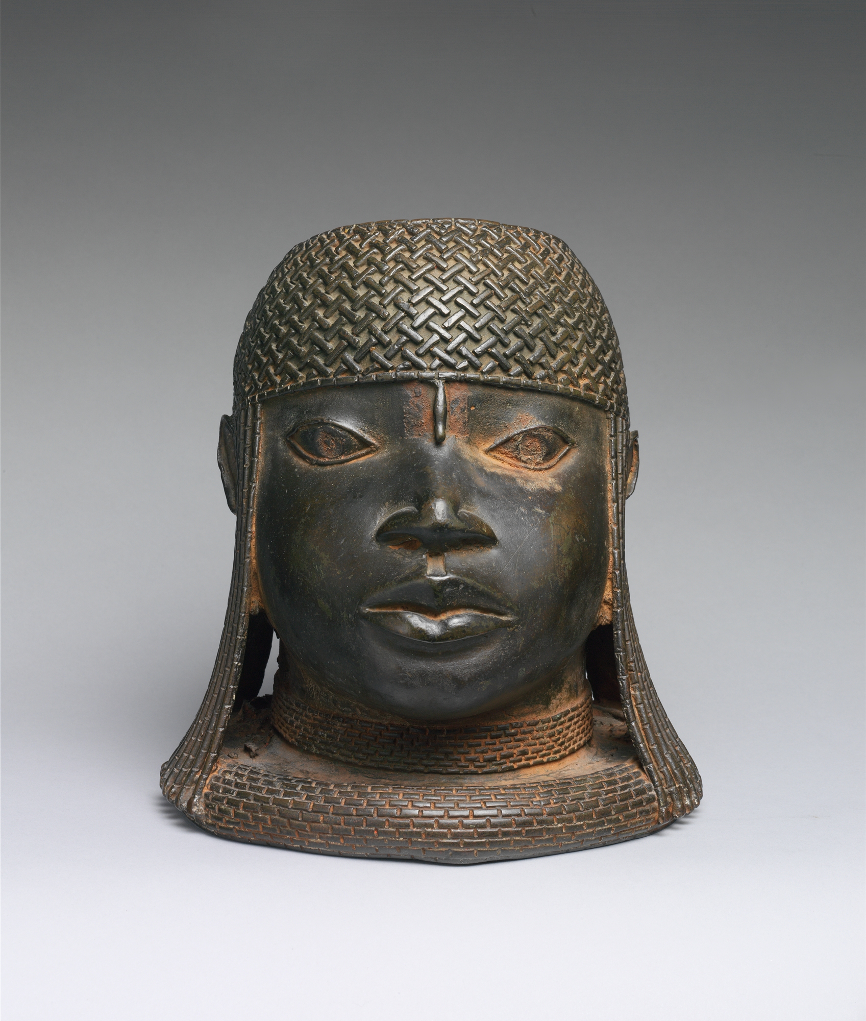 A cast bronze head of a Benin royalty with long hair wearing a straw hat