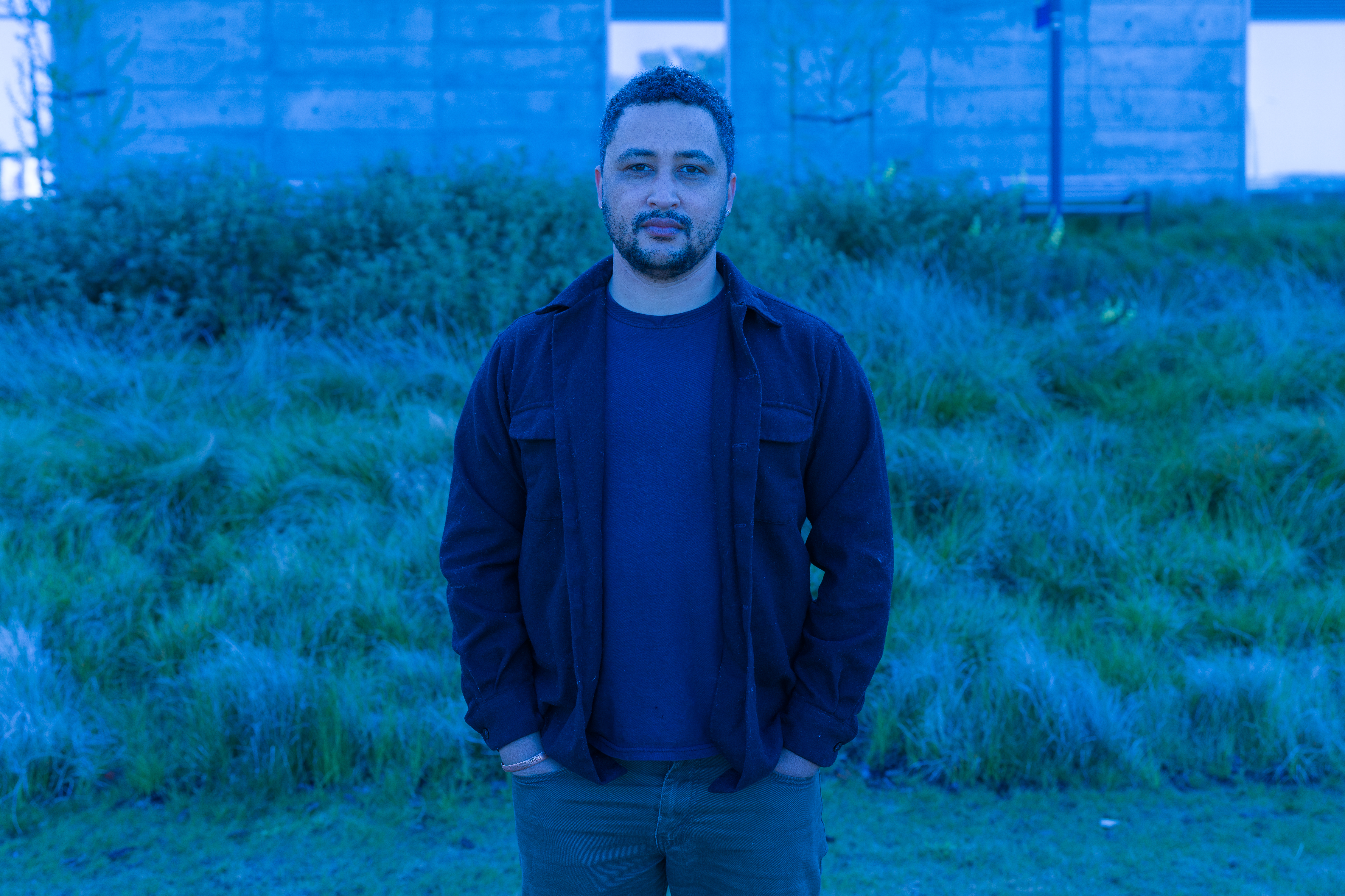 Man standing in front of a grassy hill and everything appears with a blue tint.