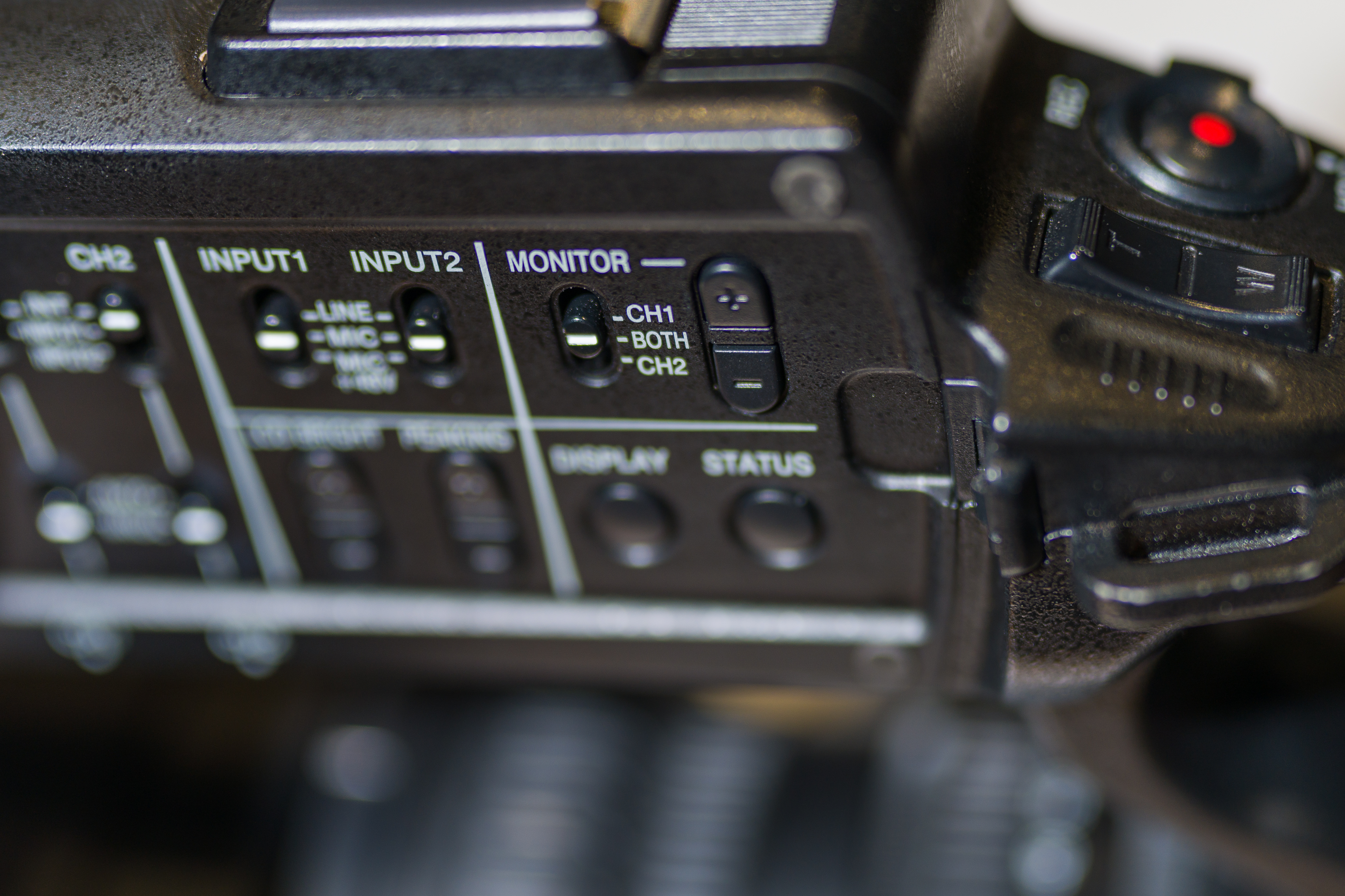 Audio headphone controls on a video camera. There are volume buttons and a switch for channel 1, channel 2, or both.