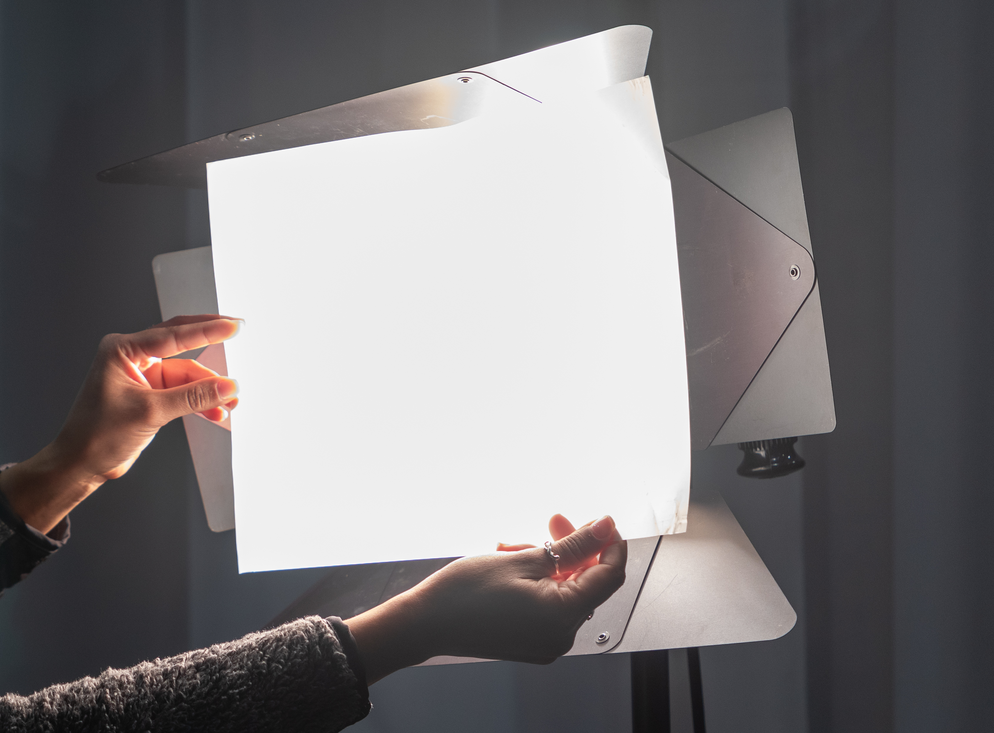 A person holding a diffusion gel in front of a hard light making the light softer. 