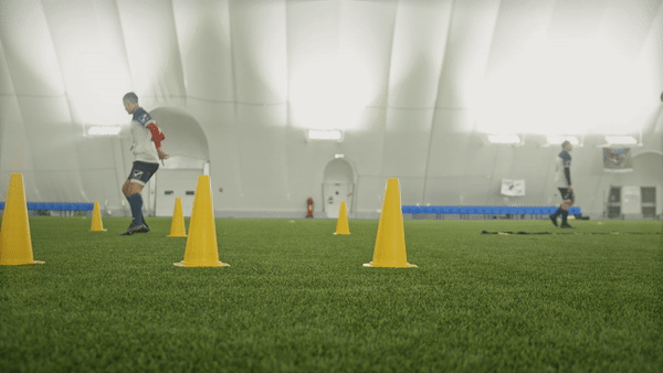 The camera following a side view of a man running between cones for soccer practice.